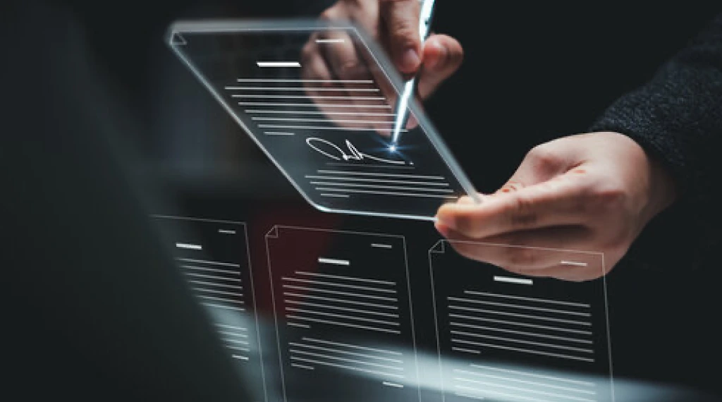 A person signing a digital document on a transparent tablet with a stylus.