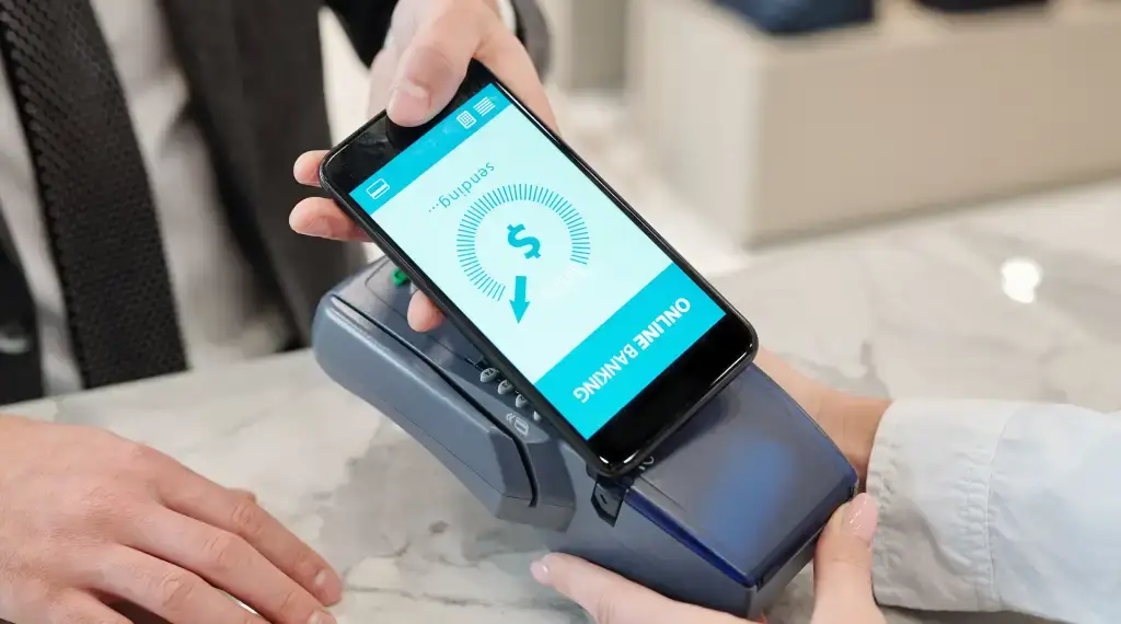 Mobile payment being processed via a smartphone on a point-of-sale terminal, representing digital deposits.