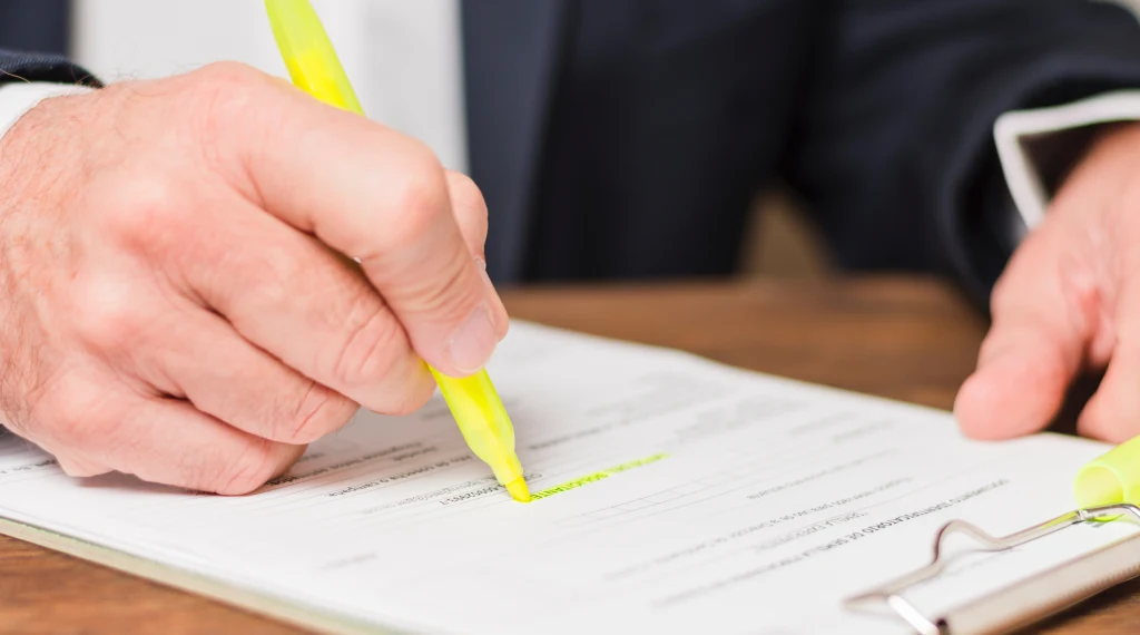 Close-up of a person highlighting text on a document, emphasizing the importance of reading terms and conditions.