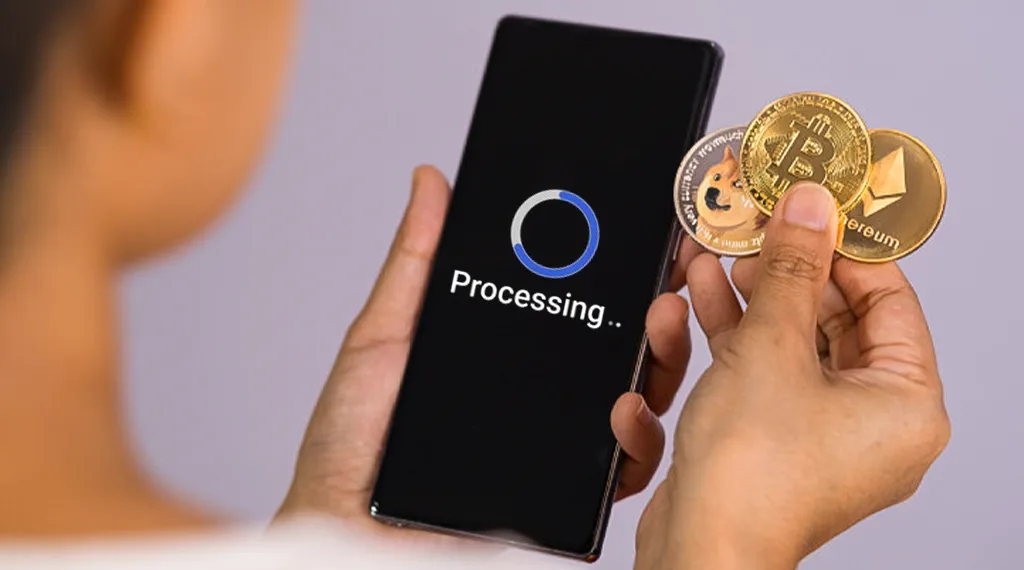 Hand holding Dogecoin, Bitcoin, and Ethereum while phone processes transaction.