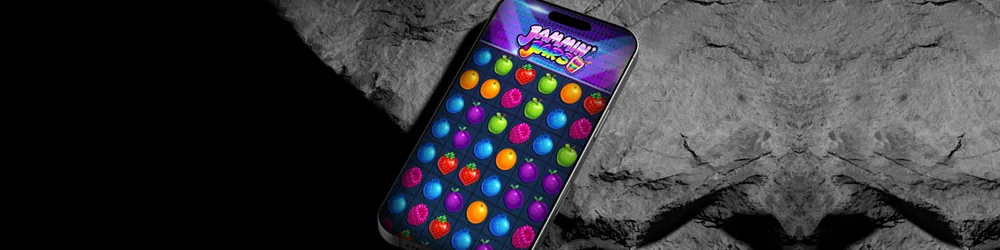 A smartphone displaying the vibrant Jammin' Jars slot game, featuring a grid of colorful fruits like grapes, oranges, and apples. The game interface is bright and eye-catching, with the colorful fruits arranged in a fun, playful manner.