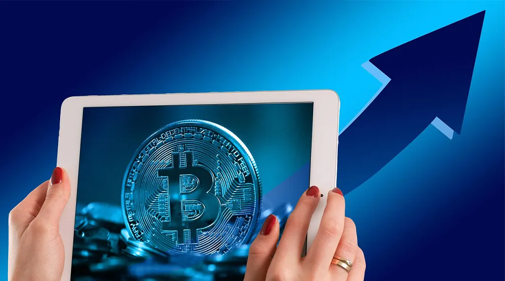 Hand holding a tablet displaying a Bitcoin coin with an upward arrow symbolizing growth.