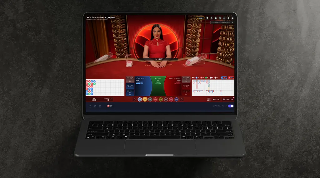 オンラインカジノのスピードバカラゲームをプレイしているラップトップ。ディーラーが赤いドレスを着て、テーブルにはゲームの進行状況が表示されています。